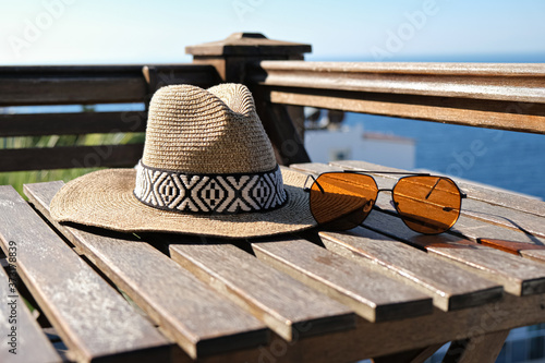 Fototapeta Naklejka Na Ścianę i Meble -  straw hat with sunglasses with on wooden terrace of holiday villa or hotel with sea view
