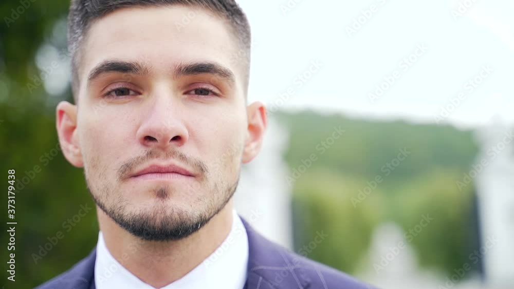 close-up portrait of a young attractive man with a beard in a suit and tie. looks away and into the camera. Stylish fashion groom on the outside. Fashion confident businessman standing alone. Wedding close-up portrait of a young attractive man with a beard in a suit and tie. looks away and into the camera. Stylish fashion groom on the outside. Fashion confident businessman standing alone. Wedding