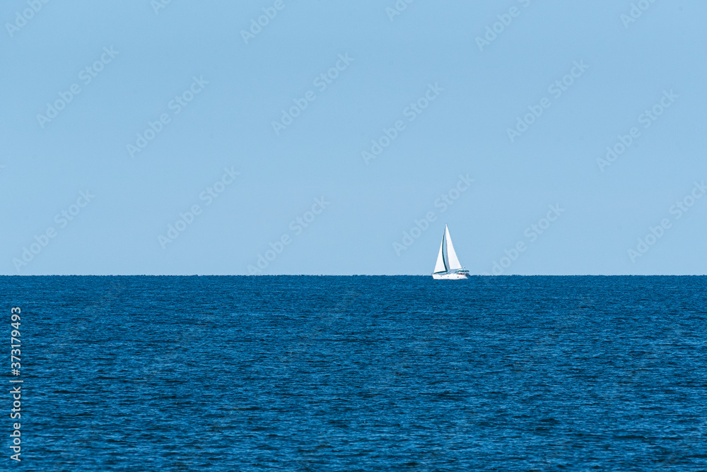 White sailboat sailing on calm blue water near horizon