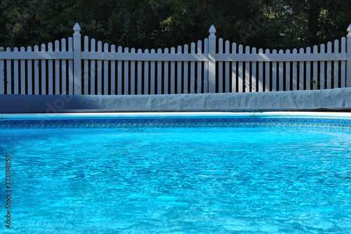 Backyard swimming pool by white vinyl fence and trees