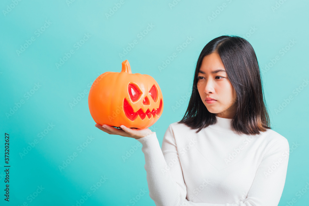 Portrait of Asian beautiful young woman holding orange model pumpkins, funny happy female with ghost pumpkins, studio shot isolated on blue background Portrait of Asian beautiful young woman holding orange model pumpkins, funny happy female with ghost pumpkins, studio shot isolated on blue background
