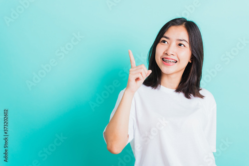 Portrait of Asian teen beautiful young woman smile have dental braces on teeth laughing point finger side away blank copy space  studio shot isolated on blue background  medicine and dentistry concept