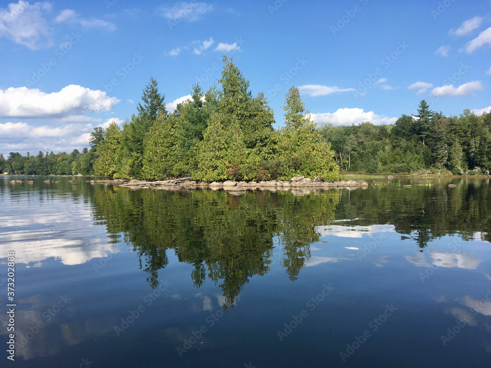 Fototapeta premium Trees reflected in the water at McGrath Pond, a pretty lake in Maine on a sunny day with clouds