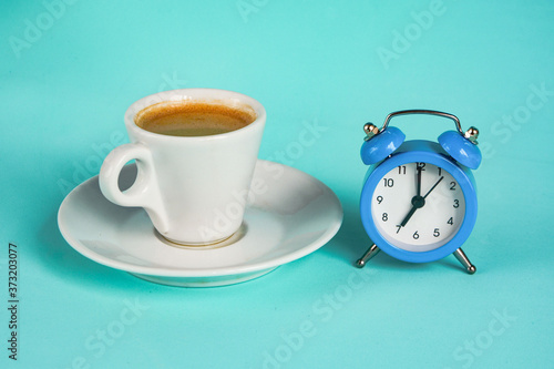 Cup of coffee, espresso and blue alarm clock on blue background close up.7 a.m., Morning concept.