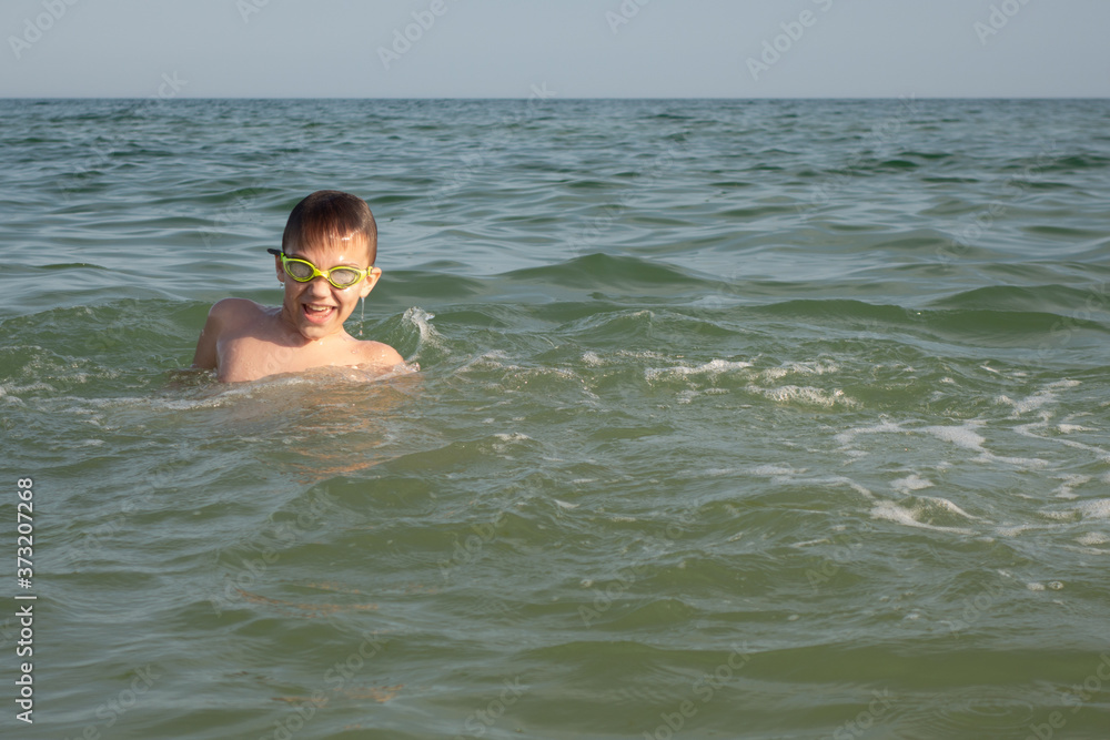 Boy 10 years old in green swimming goggles bathes in the sea.