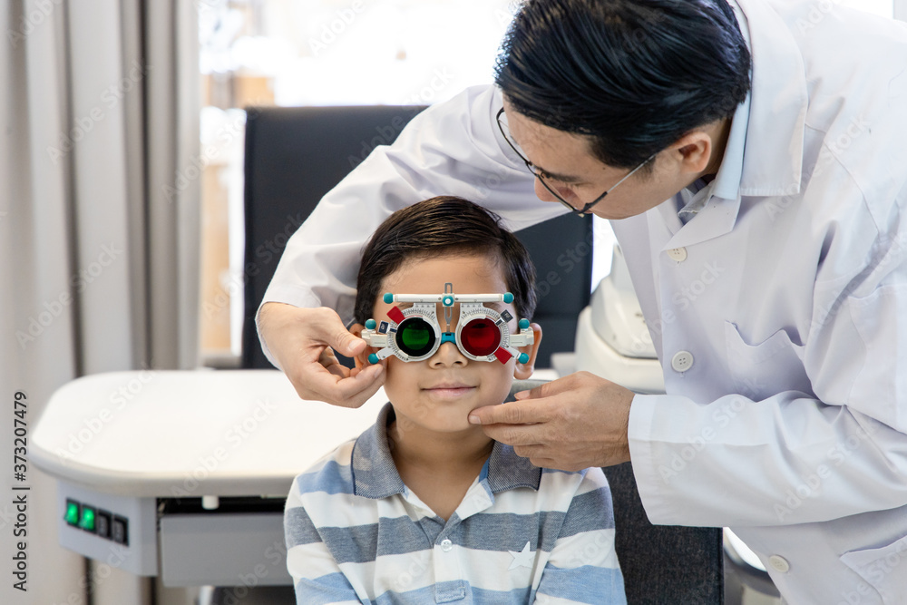 An Asian optometrist examines a child's eyesight using a Trial Frame. The boy patient visits an ophthalmology clinic.