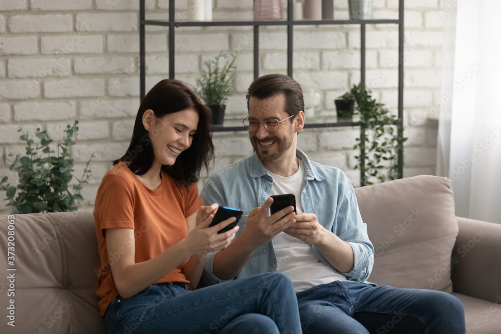 Happy young Caucasian couple sit relax on sofa at home use smartphones gadgets together, smiling millennial man and woman rest on couch in living room have fun browsing cellphone, technology concept Happy young Caucasian couple sit relax on sofa at home use smartphones gadgets together, smiling millennial man and woman rest on couch in living room have fun browsing cellphone, technology concept