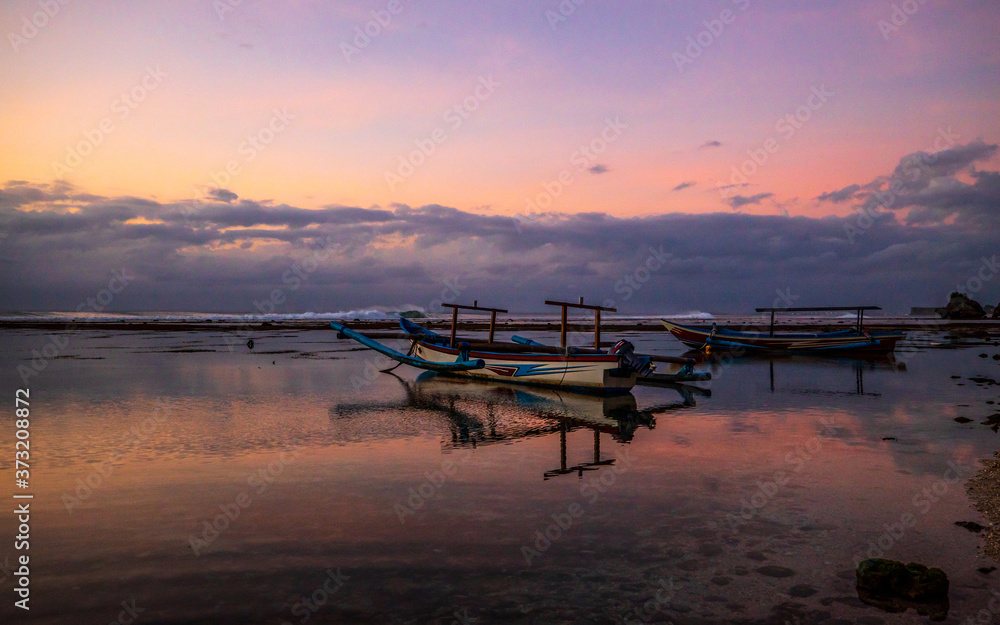 Seascape. Fisherman boat jukung. Traditional fishing boat at the beach during sunset. Cloudy sky. Amazing water reflection. Thomas beach, Bali