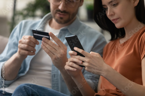 Crop close up of young couple make online purchase payment on cellphone pay with credit card, millennial man and woman shopping on internet on smartphone, use secure banking service system on gadget