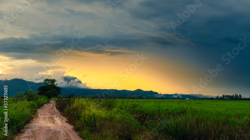 The beautiful landscape, The Twilight time sunset with colorful Rain clouds, A dirt road leading to the mountains The sun's rays through at the top of the hill and the rain, Northern Thailand