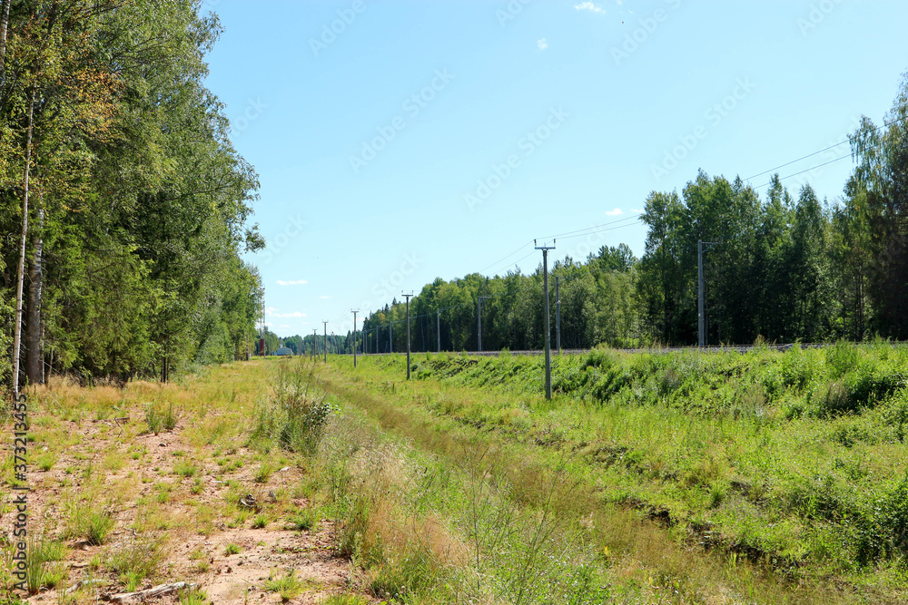 railroad tracks in the countryside surrounded by forest under bright blue summer sky railroad tracks in the countryside surrounded by forest under bright blue summer sky