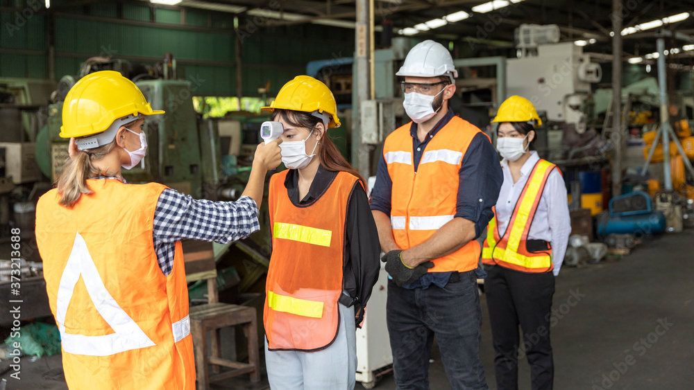 Factory in new normal. Worker uses infrared thermometer measuring temperature with staff scanning for Coronavirus or Covid-19 symptom at factory entrance. International medical healthcare system Factory in new normal. Worker uses infrared thermometer measuring temperature with staff scanning for Coronavirus or Covid-19 symptom at factory entrance. International medical healthcare system