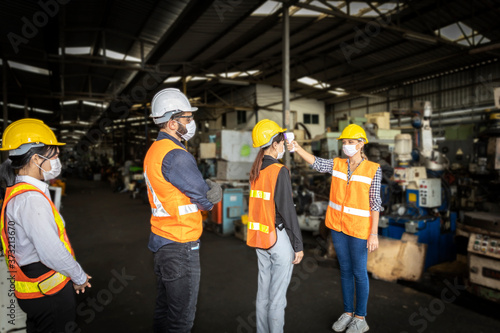 Factory in new normal. Worker uses infrared thermometer measuring temperature with staff scanning for Coronavirus or Covid-19 symptom at factory entrance. International medical healthcare system