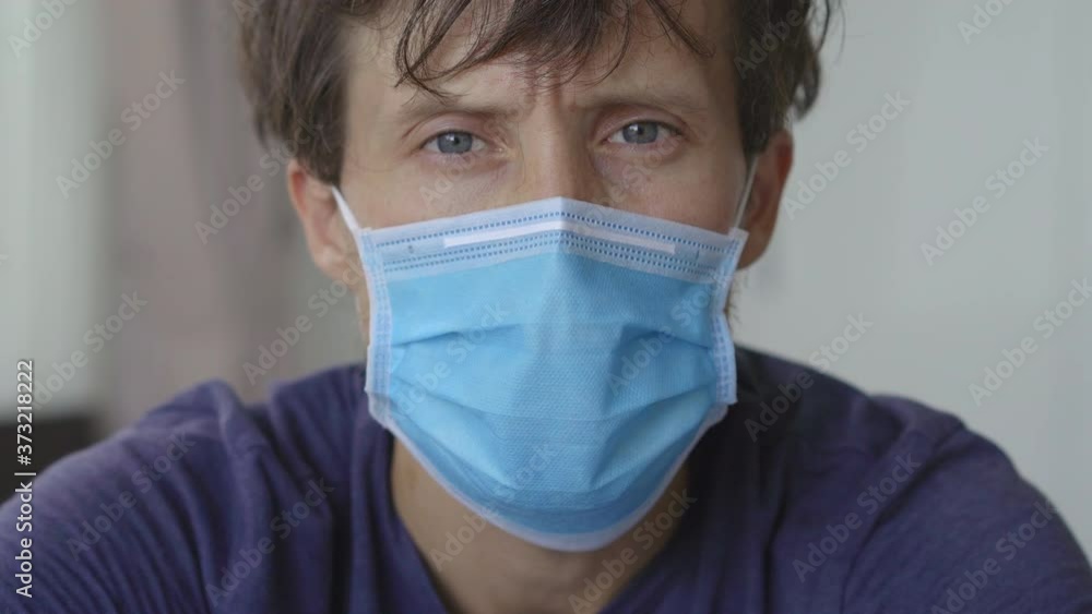 Closeup shot of a young man in mandatory quarantine. He stays in one room for two weeks. He wears a facemask, he is stressed and upset. Staying in quarantine concept. Concept of the second wave of Closeup shot of a young man in mandatory quarantine. He stays in one room for two weeks. He wears a facemask, he is stressed and upset. Staying in quarantine concept. Concept of the second wave of