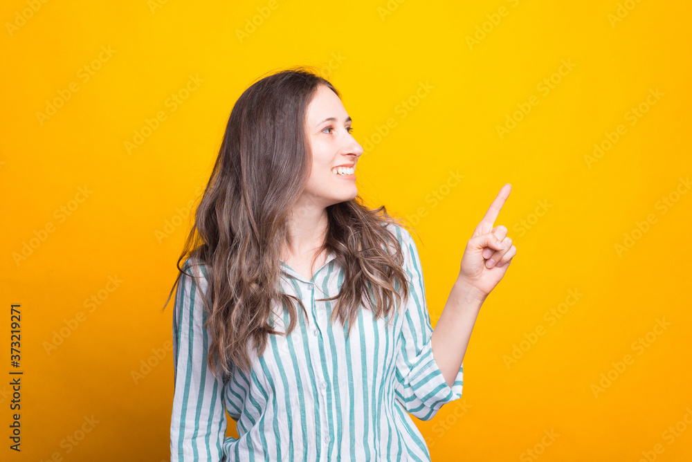 Cute smiling young woman is pointing aside over yellow background. Cute smiling young woman is pointing aside over yellow background.