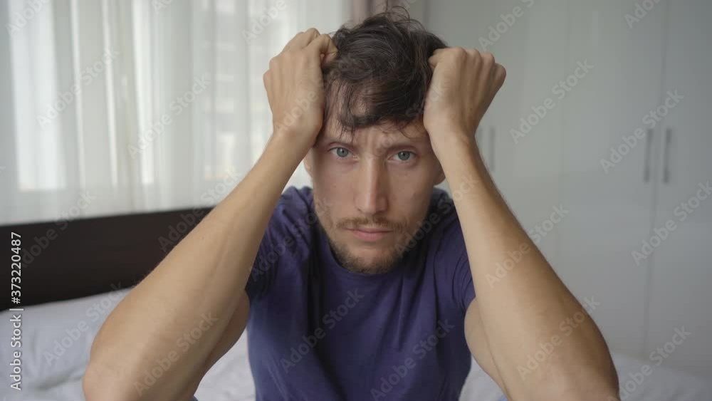 Closeup shot of a young man in mandatory quarantine. He stays in one room for two weeks. He did not shave for a long time, he needs a haircut. He is stressed and upset. Staying in quarantine concept Closeup shot of a young man in mandatory quarantine. He stays in one room for two weeks. He did not shave for a long time, he needs a haircut. He is stressed and upset. Staying in quarantine concept