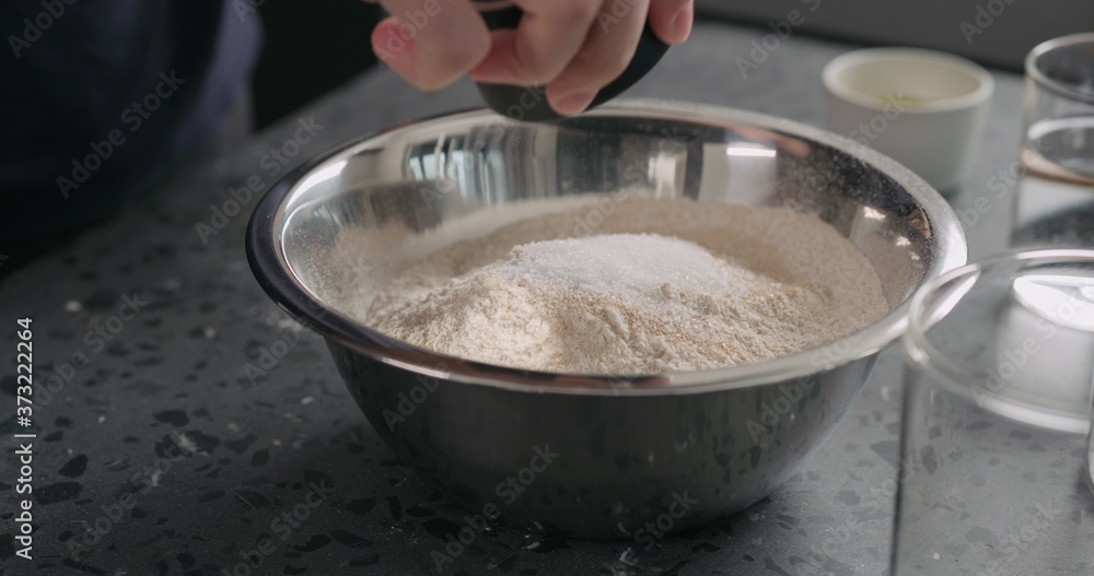 add dry ingredients into flour in steel bowl on concrete countertop add dry ingredients into flour in steel bowl on concrete countertop