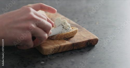man hand spreading cream cheese on slice of ciabatta