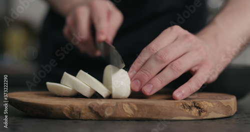 man slicing fresh mozzarella cheese on olive wood board