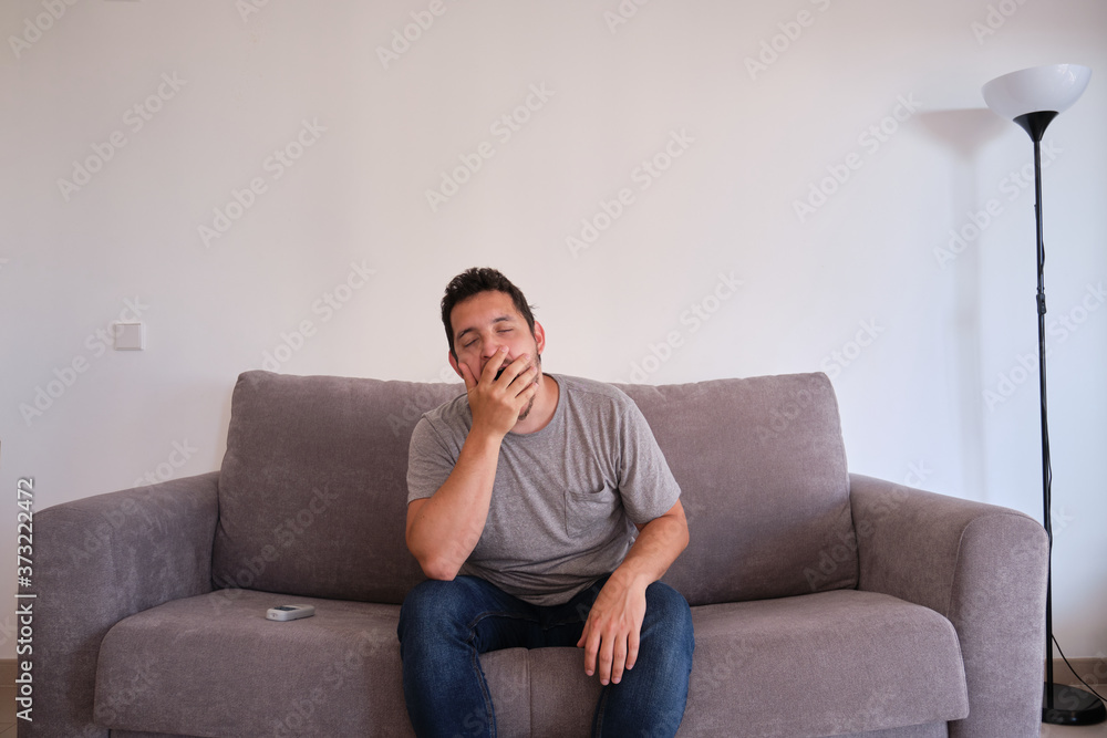 Portrait of a bored and tired young man sitting on a sofa yawning. Fatigue and tiredness concepts. Portrait of a bored and tired young man sitting on a sofa yawning. Fatigue and tiredness concepts.