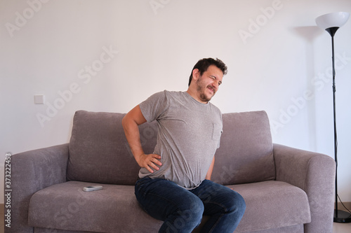 Young man sitting on a sofa suffering from low back pain. Backache concept.