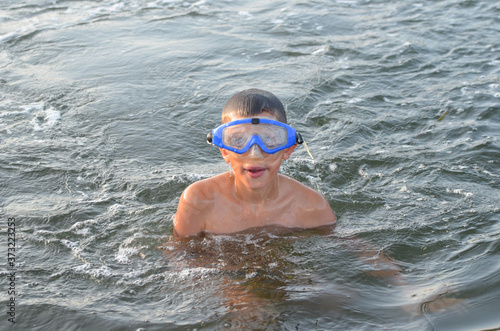 caucasian child with brown hair outdoor on the beach in summer dives in the sea with swimming mask © Marina Shvedak