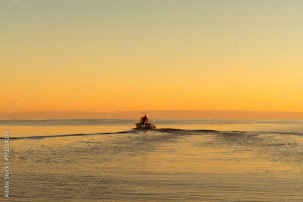Fisherman on boat at the sunset. Beautiful sunset with the fishing boat. Fishing motor boat with angler. Ocean sea water wave reflections at the sunset. Motor boat in the ocean.