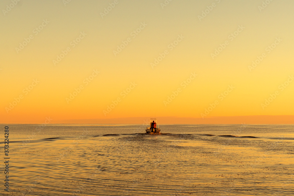 Fisherman on boat at the sunset. Beautiful sunset with the fishing boat. Fishing motor boat with angler. Ocean sea water wave reflections at the sunset. Motor boat in the ocean.
