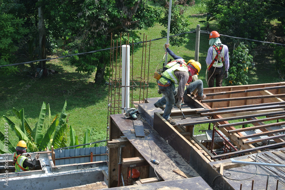 MELAKA, MALAYSIA -APRIL 6, 2016: Construction workers wearing safety harness and adequate safety gear while working at high level at the construction site in Melaka, Malaysia. MELAKA, MALAYSIA -APRIL 6, 2016: Construction workers wearing safety harness and adequate safety gear while working at high level at the construction site in Melaka, Malaysia.
