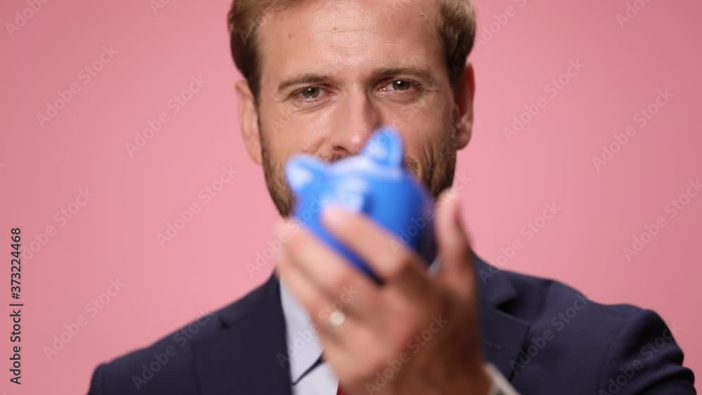 elegant businessman in suit holding piggy bank and showing, smiling and standing on pink background elegant businessman in suit holding piggy bank and showing, smiling and standing on pink background