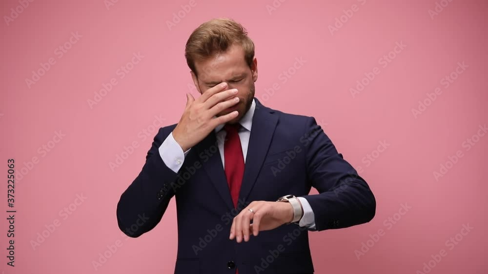 upset young businessman looking down and checking time, being late, face palming, looking up and nodding, disapproving on pink background upset young businessman looking down and checking time, being late, face palming, looking up and nodding, disapproving on pink background