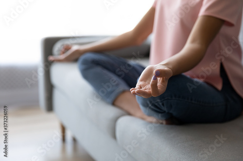 Crop close up of woman sit on couch at home practice yoga in lotus position with mudra hands, calm relaxed female rest on sofa indoors, meditate relieve negative emotions, stress free, peace concept