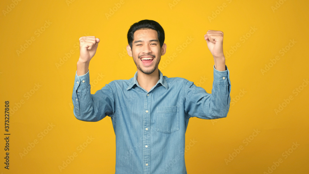 Happy asian man arm up with successful achievement while standing over isolated yellow background Happy asian man arm up with successful achievement while standing over isolated yellow background