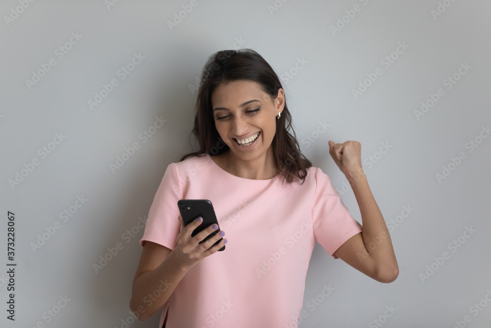 Excited young ethnic woman isolated on grey studio background look at cellphone screen celebrate online lottery win, overjoyed happy female feel euphoric triumph read good promotion news on smartphone Excited young ethnic woman isolated on grey studio background look at cellphone screen celebrate online lottery win, overjoyed happy female feel euphoric triumph read good promotion news on smartphone