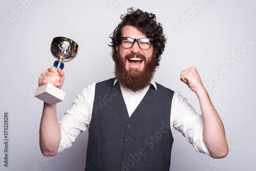 Portrait of amazed bearded hipster man in suit holding CUP and celebrating. © Vulp