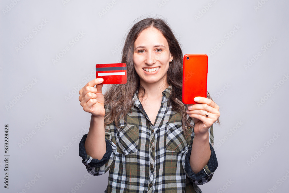 Photo of young smiling woman showing red credit card and smartphone. Photo of young smiling woman showing red credit card and smartphone.