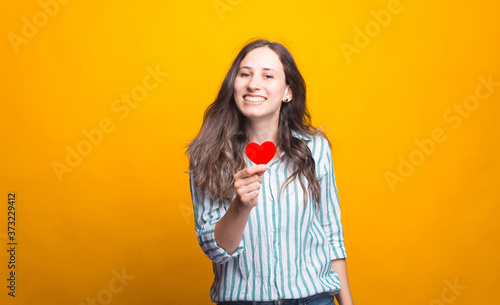 Portrait of cheerful young woman smiling and holding red paper heart.