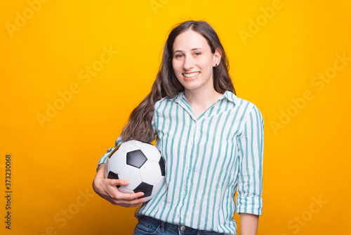 Photo of smiling young woman holding soccer ball over yellow background. © Vulp