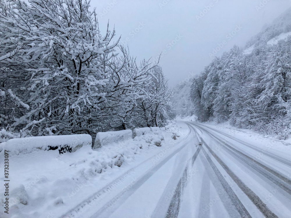 Obraz premium The road along a snow-covered serpentine road in the mountains during a blizzard. Even with a minimum speed, such a trip is very dangerous at any moment an avalanche can break out
