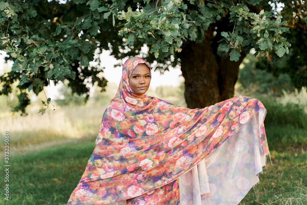 Muslim black woman African ethnicity weared traditional colorful hijab smiles under green tree. Arabic islam religion clothes. Pretty black girl smiles. Business for black woman. Muslim black woman African ethnicity weared traditional colorful hijab smiles under green tree. Arabic islam religion clothes. Pretty black girl smiles. Business for black woman.