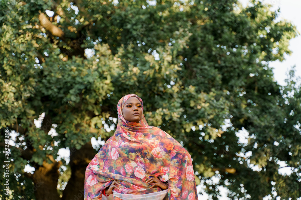 Attractive muslim black girl weared in hijab smiles and looks right side. African woman in national colorful dress on green background. Life style of black girl wearing in scarf named hijab Attractive muslim black girl weared in hijab smiles and looks right side. African woman in national colorful dress on green background. Life style of black girl wearing in scarf named hijab