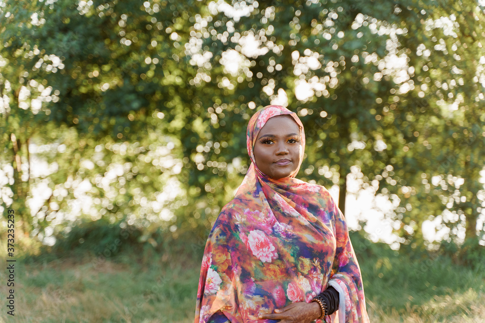 Confident muslim black girl weared in hijab smiles. African woman in national colorful dress on green background. Life style of black girl wearing in scarf named hijab. On-line work for black people Confident muslim black girl weared in hijab smiles. African woman in national colorful dress on green background. Life style of black girl wearing in scarf named hijab. On-line work for black people