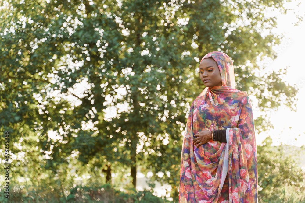 Attractive muslim black girl weared in hijab smiles and looks left side. African woman in national colorful dress on green background. Life style of black girl wearing in scarf named hijab Attractive muslim black girl weared in hijab smiles and looks left side. African woman in national colorful dress on green background. Life style of black girl wearing in scarf named hijab