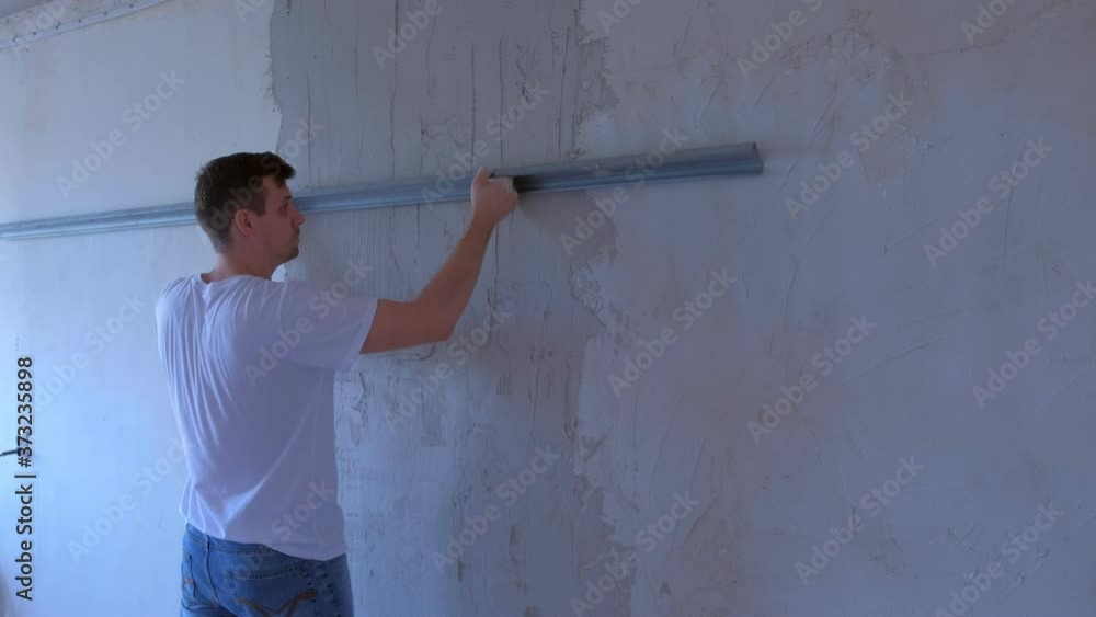 Plasterer man is aligning wet plaster on wall using long metal tool spatula. Finishing construction renovation works in apartment. Worker builder making overhaul applying grey cement putty on wall. Plasterer man is aligning wet plaster on wall using long metal tool spatula. Finishing construction renovation works in apartment. Worker builder making overhaul applying grey cement putty on wall.