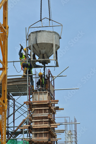 JOHOR, MALAYSIA -MAY 06, 2016: A group of construction workers pouring concrete using concrete bucket into the column formwork at the construction site. 