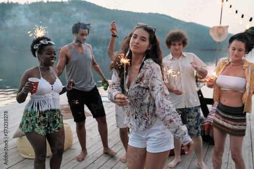 Young woman dancing with sparklers on a pier among her friends at the party outdoors