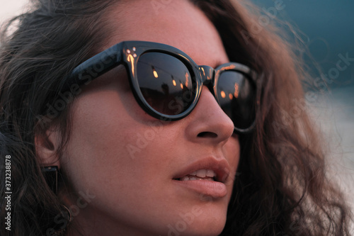 Close-up of young beautiful woman with curly hair in sunglasses standing outdoors