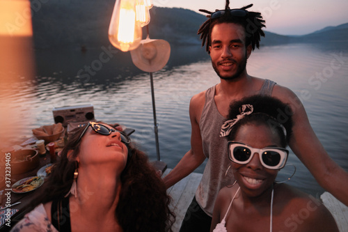Young happy people standing on a pier and smiling at camera during the party on fresh air