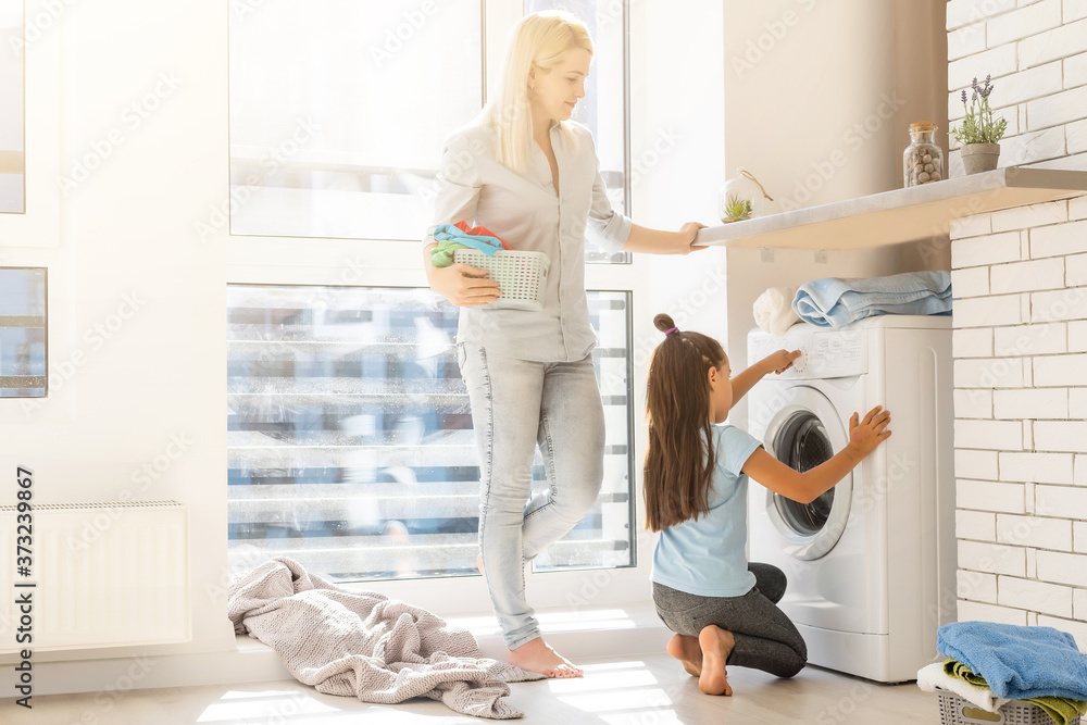 Fototapeta premium family mother and child girl little helper in laundry room near washing machine and dirty clothes