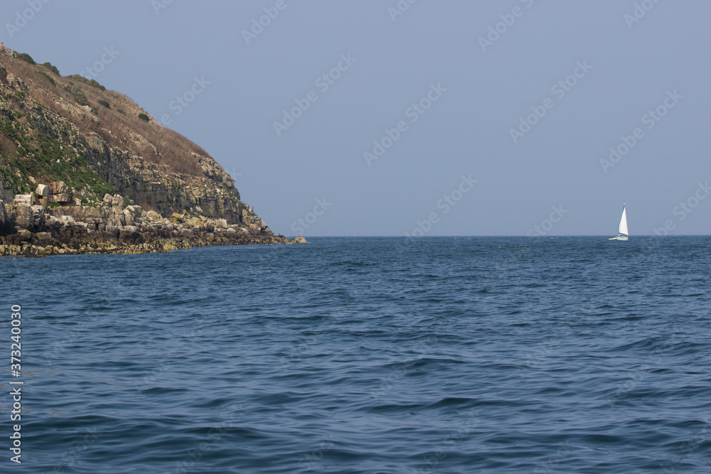 Summer day on the water at puffin Island in the Menai straits, Anglesey. Small sailing boat next to a rocky cliff.